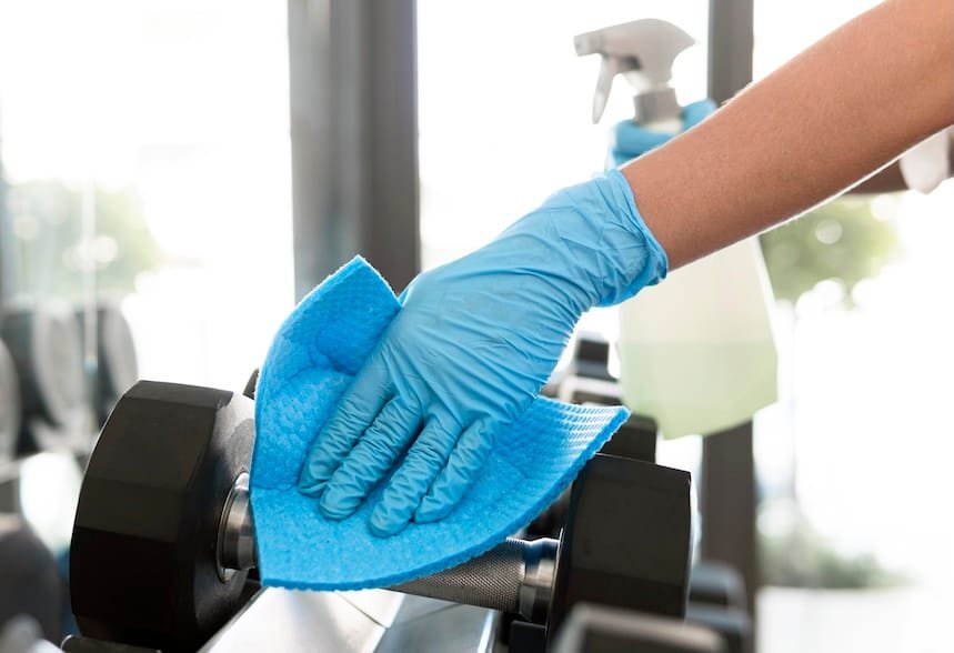 Person cleaning gym equipment with blue cloth.